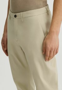 Pantalones beige ajustados con una textura suave, que cuentan con un cierre de un solo botón y bolsillos laterales, diseñados para un ajuste ceñido.