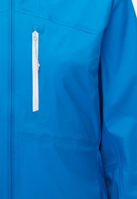 Giacca impermeabile blu con texture liscia, dotata di una tasca con zip bianca sul petto e un design delle spalle senza cuciture.