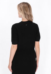Sort ribbet sweater med korte ærmer og tætsiddende design, som har et struktureret stof og et lille logo på bagsiden.