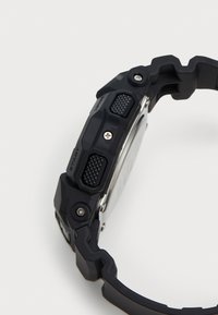 Montre numérique noire avec un bracelet en caoutchouc texturé, un cadran rectangulaire, des boutons proéminents avec des motifs de prise et des accents en acier inoxydable.