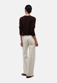 Pull en maille marron à manches longues, associé à un pantalon ample blanc à jambes larges. Détails notables des poches arrière sur le pantalon.