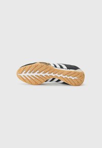 Black athletic shoe sole with a gum rubber bottom, featuring white stripes and a textured pattern for traction.