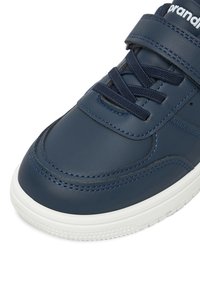 Zapatilla deportiva azul marino con suela blanca, detalles cosidos, cordones azules marinos y una correa de velcro en la parte superior delantera.