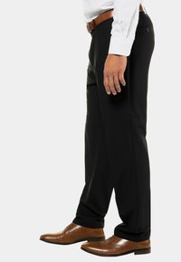 Pantalones negros de tejido suave, con un corte ajustado. Combinados con zapatos de cuero marrón y un cinturón marrón, complementados con una camisa blanca.