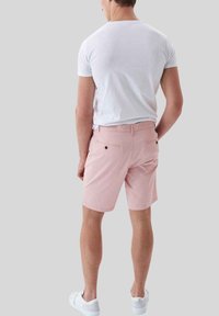 Pantalones cortos rosas con un ajuste relajado, lazos para cinturón y dos bolsillos traseros. Combinados con una camiseta blanca ajustada y zapatos blancos.