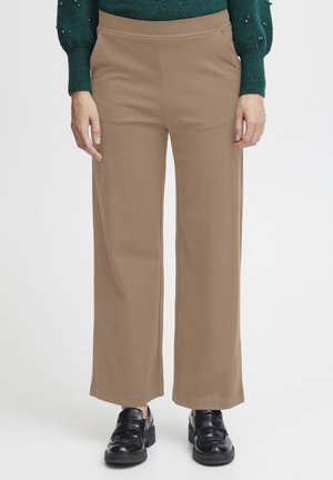 Beige vida byxor i mjukt material med en figursydd midja. I kombination med svarta skor och en mörkgrön texturerad tröja.