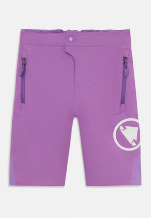 Pantalones cortos morados hechos de una tela suave y elástica. Presentan dos bolsillos con cremallera y un logo circular en la pierna derecha.