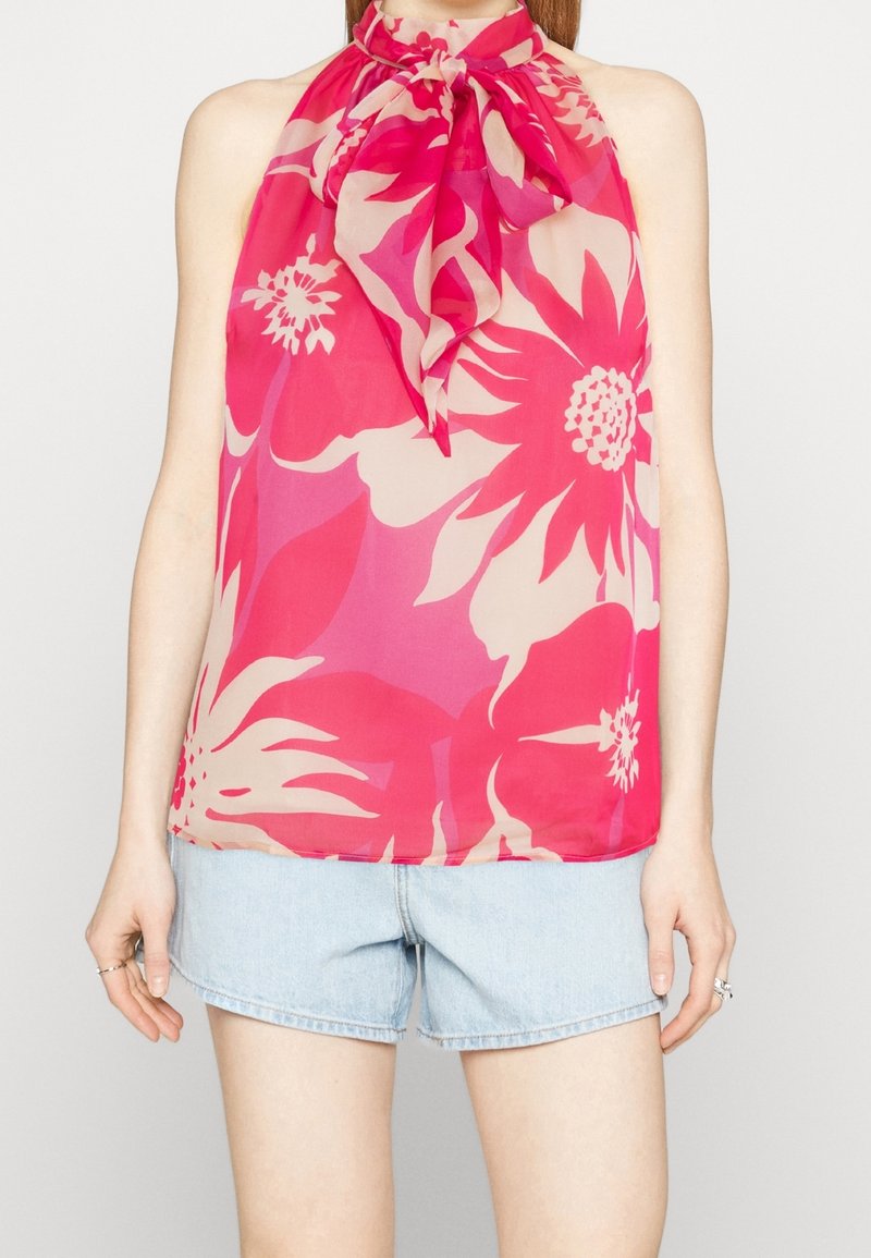 Femme portant un haut à bretelles fleuri rose et rouge avec un nœud au cou, associé à un short en denim bleu clair.