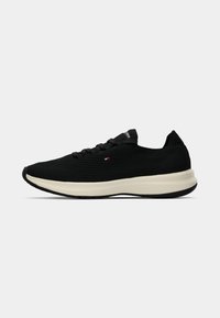 Black athletic shoes with a textured mesh upper, lace-up design, and cream-colored midsole. Features a small logo detail on the side.