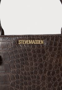 Smeđa torba od umjetne kože s teksturom krokodila, s zlatnim logotipom "STEVE MADDEN" kao istaknutim akcentom.