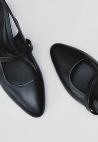 Zapatos de cuero negro con puntera puntiaguda y corte curvado. Presentan tiras delgadas en el tobillo y una textura suave. Diseño elegante, estilo minimalista.