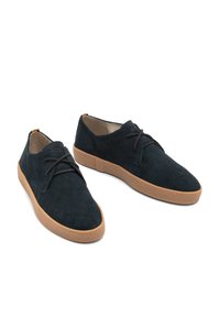 Sötétkék velúr cipők texturált felszínekkel, kerek orral és barna gumitalppal; fekete cipőfűzőkkel és színes díszítésekkel a saroknál.