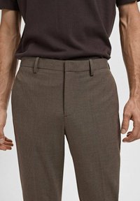 Brown patterned trousers with a slim fit, featuring belt loops and a flat front design. The fabric has a fine texture, complementing a casual look.