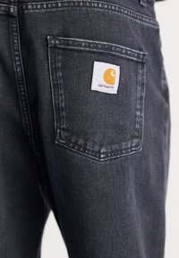Mustat denimin farkut lähikuvassa, jossa näkyy takatasku, jossa on valkoinen Carhartt-logo
