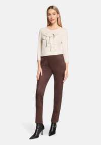 Długi top w jasnobeżowym kolorze z napisem "STYLE", zestawiony z dopasowanymi ciemnobrązowymi zamszowymi spodniami i czarnymi szpilkami z zaostrzonymi czubkami.