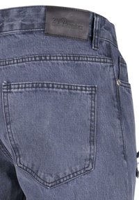 Traperice tamnog pranja s detaljem izbliza na stražnjem džepu. Sadrži kožni tag i klasično šivanje.