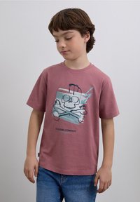 Różowy bawełniany t-shirt z grafiką czaszki i skrzyżowanych kości w kolorach niebieskim i czarnym, z napisem "SCALPERS COMPANY" poniżej.