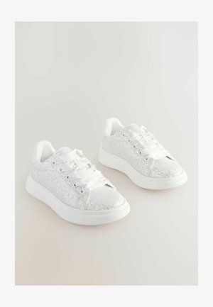 Fehér csillogó sportcipők sima fehér fűzőkkel, lekerekített orral és finom párnázással a nyelvnél és a bokánál. Gumitalp.