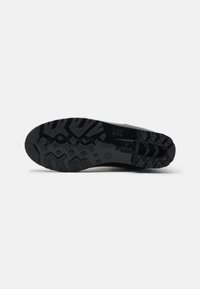 Semelle de chaussure noire avec un motif de semelle rugueux, en caoutchouc. Présente un talon plat, une surface texturée et une empreinte de logo près du centre.