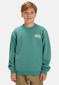 Türkisfarbene Sweatshirt, runder Halsausschnitt, gerippte Bündchen und Saum, mit goldenem Quiksilver-Logo auf der linken oberen Seite. Weicher, strukturierter Stoff.