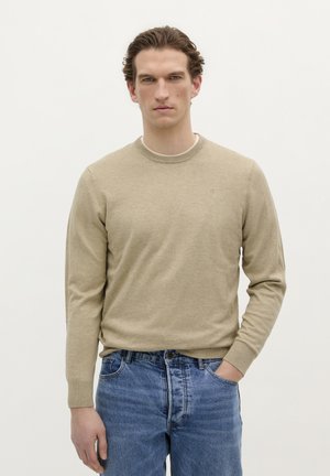 Pulover bej cu mâneci lungi, cu decolteu rotund, textură tricotată și manșete cu striații, purtat cu blugi din denim albastru.