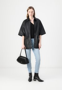 Jacket din piele neagră, cu mâneci scurte și închidere cu nasturi; asociat cu blugi de culoare bleu deschis și cizme cu toc negre până la gleznă. Include o geantă neagră.