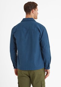 Blue, long-sleeve shirt in smooth fabric with a collar; features a square patch at the back and buttoned cuffs; paired with olive green pants.