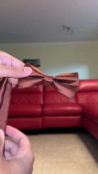 Braune Satin-Schleife, die von einer Hand gehalten wird, mit einer glatten Textur und einer klassischen Form, an der ein passendes Stoffband befestigt ist.