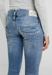 Ljusblå denimjeans med en åtsittande design, med distinkta bakfickor och en märkesetikett vid midjan. Texturerad tygfinish.