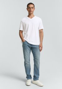 Weißes V-Ausschnitt-T-Shirt mit kurzen Ärmeln, kombiniert mit hellblauen Jeans und weißen Sneakers; legerer Schnitt mit glatter Textur.