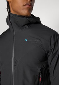 Schwarze Jacke mit hohem Kragen, ausgestattet mit einer strukturierten Oberfläche, Reißverschlusstasche und blauem Markenlogo. Schlankes Design mit modernen Akzenten.