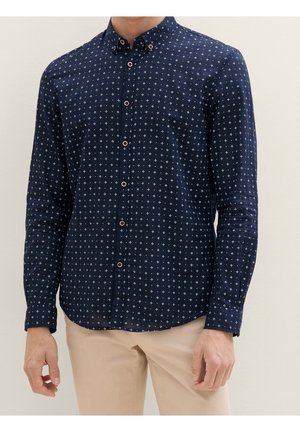 Camicia blu navy con piccoli motivi geometrici bianchi, maniche lunghe e colletto alla francese. Presenta bottoni marroni e una texture liscia.