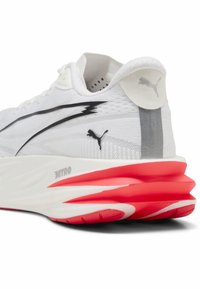 Λευκό αθλητικό παπούτσι Puma με μαύρο λογότυπο, μαύρο σχέδιο αστραπής και παχιά κόκκινη και άσπρη αποσβεσμένη σόλα με την ένδειξη "NITRO", εμφανιζόμενο από πίσω πλευρά.