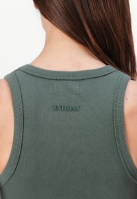 Ribbede, ermeløse grønne topp med rund hals. Har et lite brodert "2NDDAY"-logo på baksiden. Glatt tekstur.