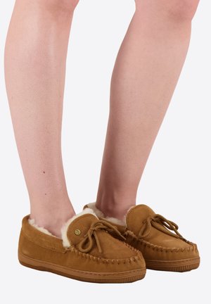 Pantoufles mocassins en daim tan avec une douce doublure en fausse fourrure, bout arrondi et nœud décoratif. Semelle en caoutchouc texturé pour une meilleure adhérence et durabilité.