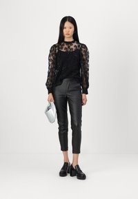 Top negro transparente con patrones florales y lentejuelas, combinado con pantalones ajustados de cuero sintético negro y zapatos de plataforma negros gruesos, sosteniendo un bolso de mano plateado.