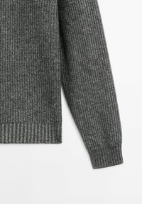 Manche et ourlet visibles d'un pull gris côtelé à manches longues sur fond blanc, mettant en valeur la texture et le motif du tricot.