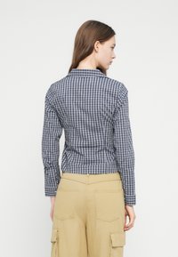 Μπλούζα με καρό navy και λευκό, με γιακά και εφαρμοστή μέση. Η πλάτη παρουσιάζει ραφές και μακριά μανίκια.