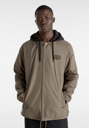 Beige letvægtsjakke med hætte, der har en frontknaplukning og et Vans-logo. Ærmerne er elastiske ved håndleddene.