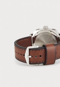 Bracelet de montre en cuir marron avec perforations, doté d'une boucle en métal argenté et d'un boîtier argenté à l'arrière. Texture lisse et design simple.