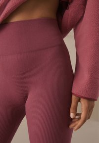 Prążkowane legginsy z wysokim stanem w głębokim różowym kolorze, zestawione z dopasowaną, puszystą kurtką, prezentujące miękką teksturę i dopasowany krój.