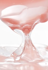 Liquide rose translucide avec une texture lisse et fluide, présentant des bulles et une finition brillante. Se forme en une forme délicate en gouttant.