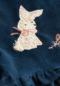 Marine stof met een witte geborduurde konijn, roze accenten en een gerimpelde rand. Opmerkelijke details zijn onder andere de getextureerde stiksel en een pluizige staart.