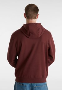 Felpa bordeaux con cappuccio regolabile, texture liscia, polsini e orlo a coste, e una vestibilità comoda. La vista posteriore mostra dettagli di design minimi.