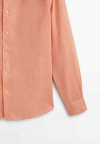 Chemise à manches longues de couleur pêche avec manches à poignets contrastant sur fond blanc.