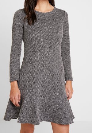 Kvinde iført en langærmet, knælange kjole med figursyet talje og sort-hvidt fiskebensmønster.