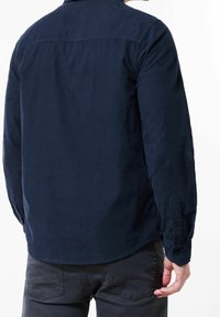 Tmavě modrá košile s dlouhým rukávem z měkké látky, s manžetou na knoflíky, zadním sedlem a zakulaceným lemem. Jednoduchý design bez vzorů.