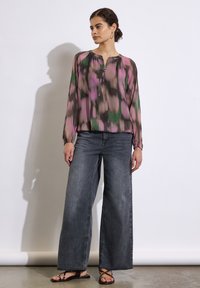 Luftig, langærmet bluse i multifarvet abstrakt mønster med lyserøde, grønne og brune nuancer. Sammen med brede grå jeans og sandaler.