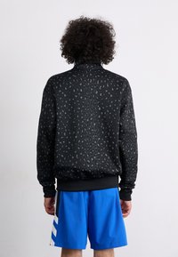 Black sweatshirt with a leopard print pattern in gray, featuring a high collar and ribbed cuffs, paired with blue shorts.