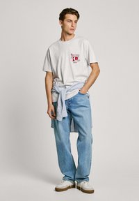 Light gray cotton t-shirt with a red graphic design, paired with light blue relaxed-fit jeans. Blue and white plaid shirt tied around the waist.